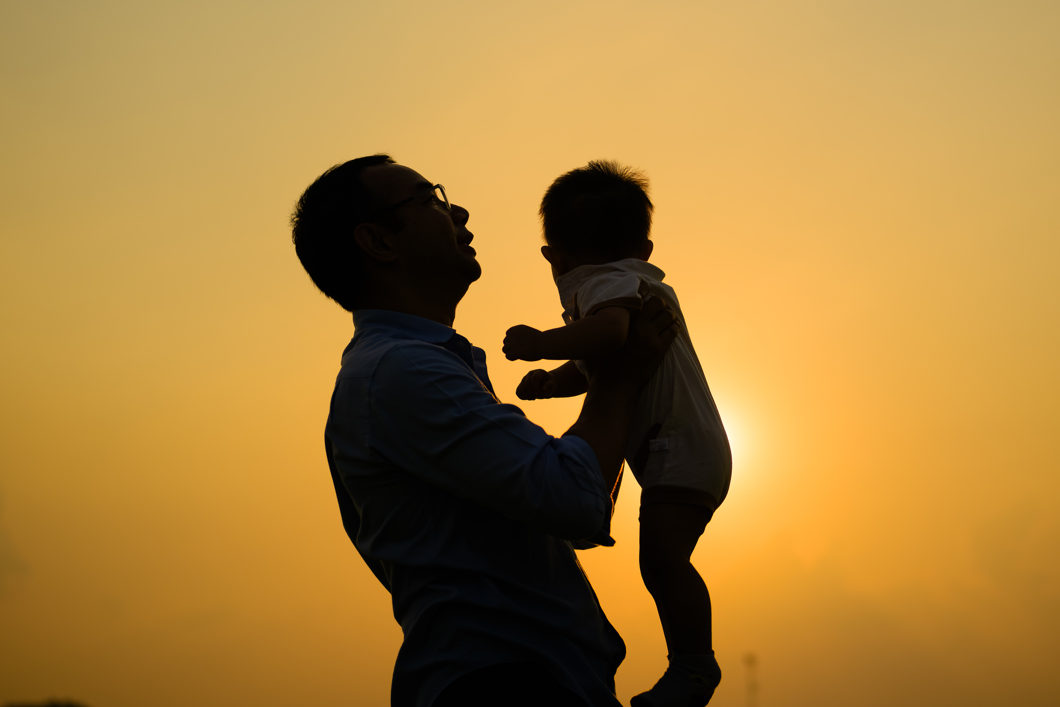 Happy father holding newborn baby playing together with sunset view